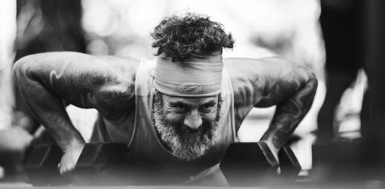 Athlète barbu et souriant faisant des pompes sur des haltères dans un gym